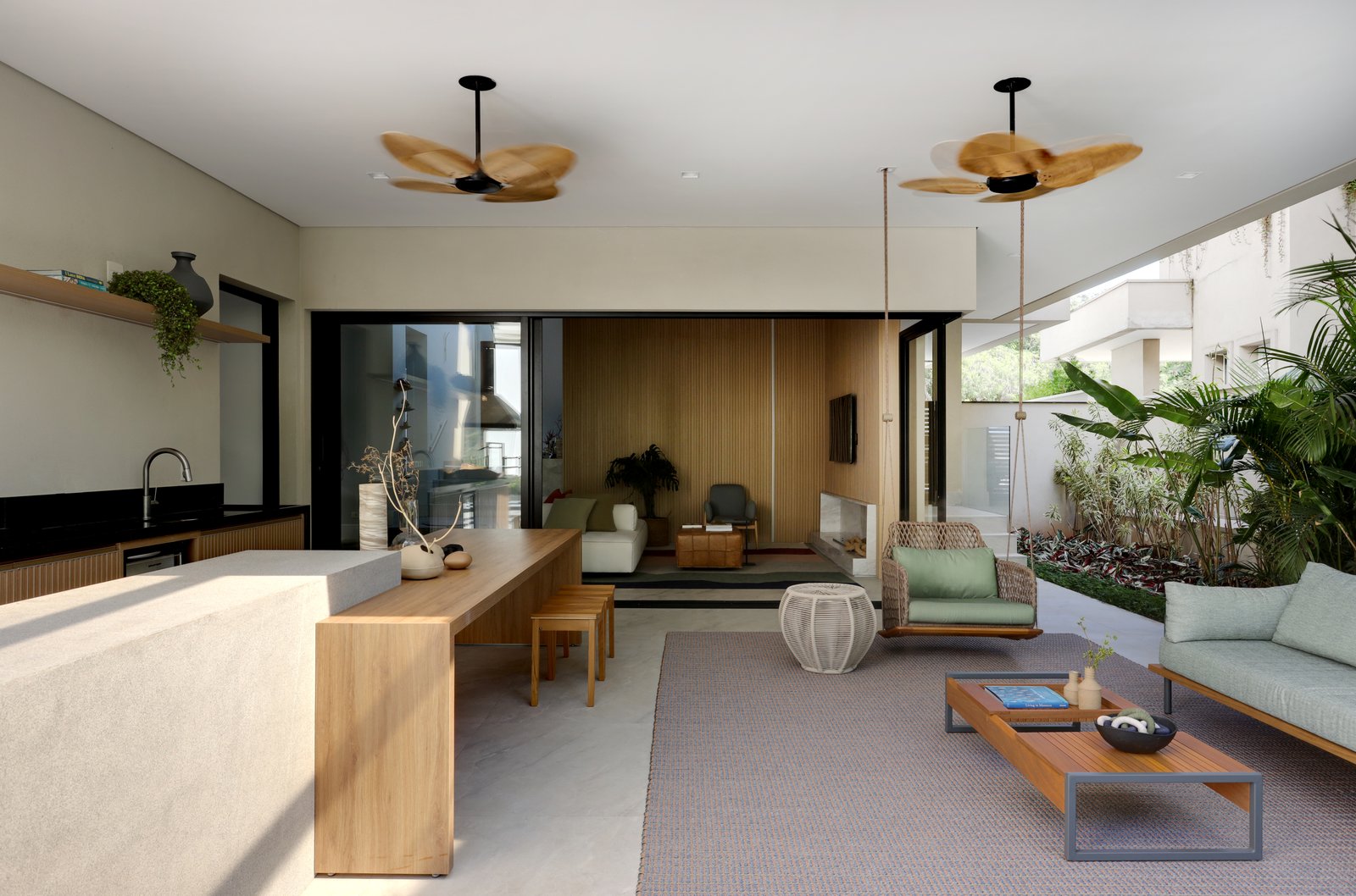 Ampla sala de estar e jantar com cozinha integrada, móveis de madeira clara e ventiladores pendentes — projeto Projeto Destaque Club&Casa, por Barbara Dundes – Arquitetura + Design
