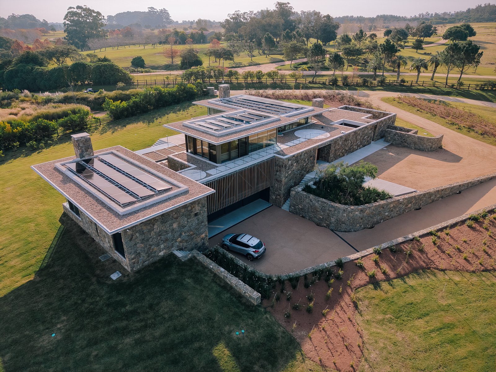 Residencia moderna con fachada de piedra y paneles solares en entorno rural — proyecto Laguna Estates, en Maldonado