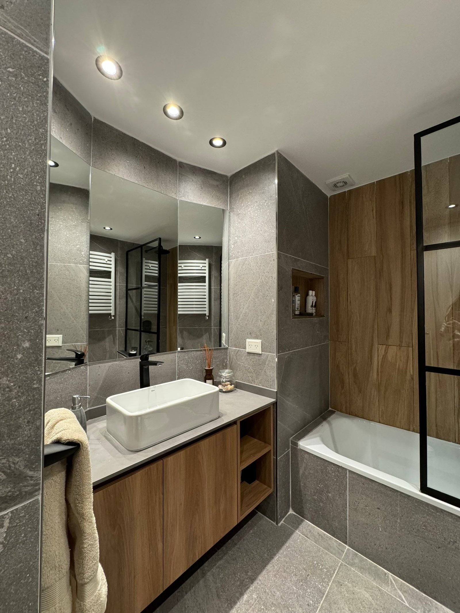 Baño moderno con revestimientos de piedra gris y mueble de madera — proyecto Salguero II, por MDBK Arquitectura, en Palermo
