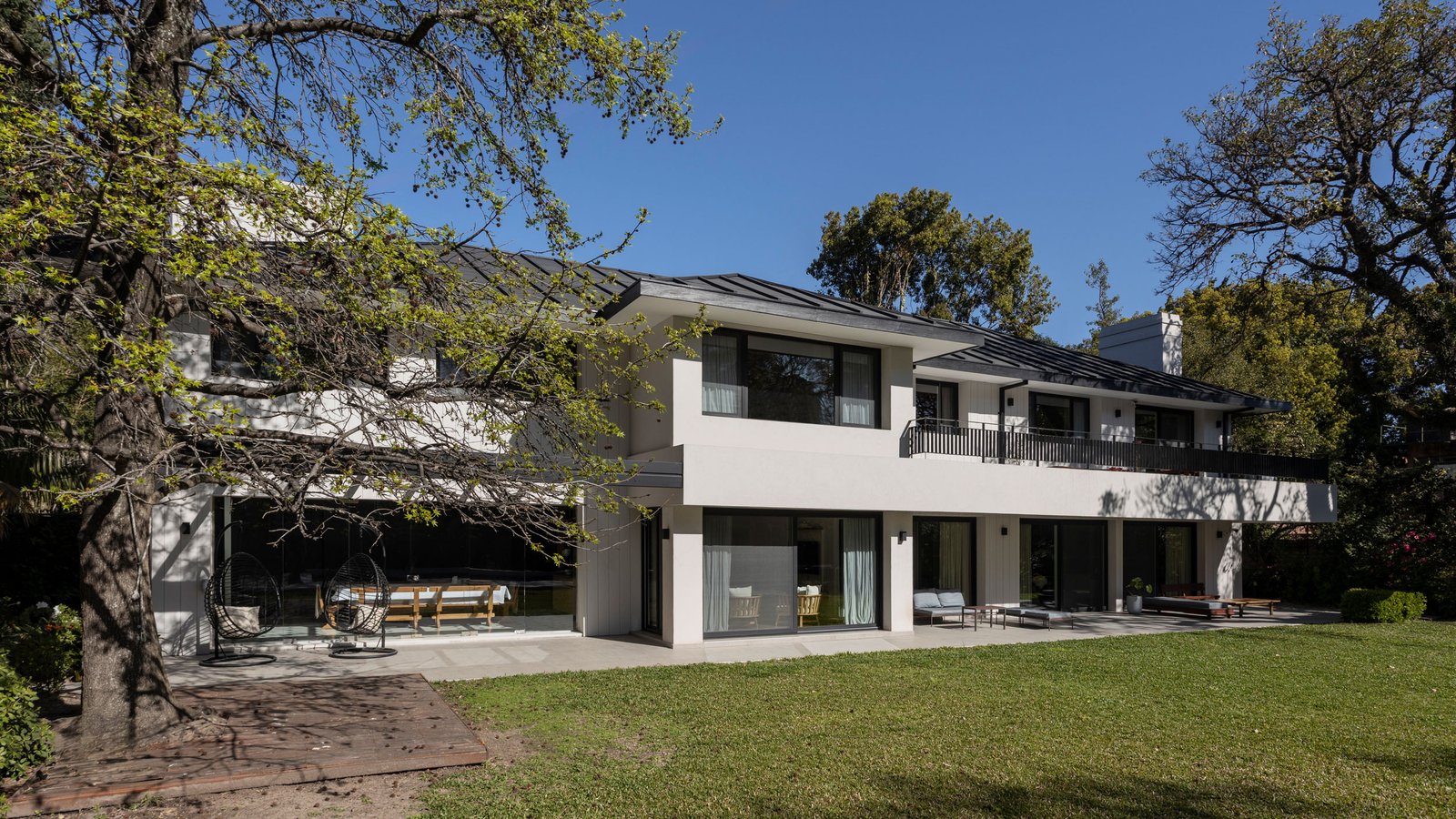 Fachada moderna con árboles maduros y deck de madera — proyecto REFORMA DG, por Rastro Estudio, en Punta Chica