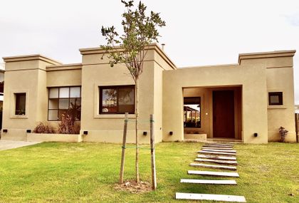 Fachada moderna de casa beige con jardín y sendero adoquinado — proyecto Santa Teresa 2, por Marconi Silva Arquitectos, en Benavidez