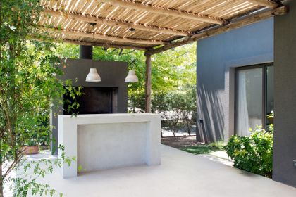 Espacio semiexterior con parrilla de hormigón, pérgola de mimbre y abundante vegetación — proyecto Roble Joven, por Estudio Arq. María Sioli, en Manuel Alberti
