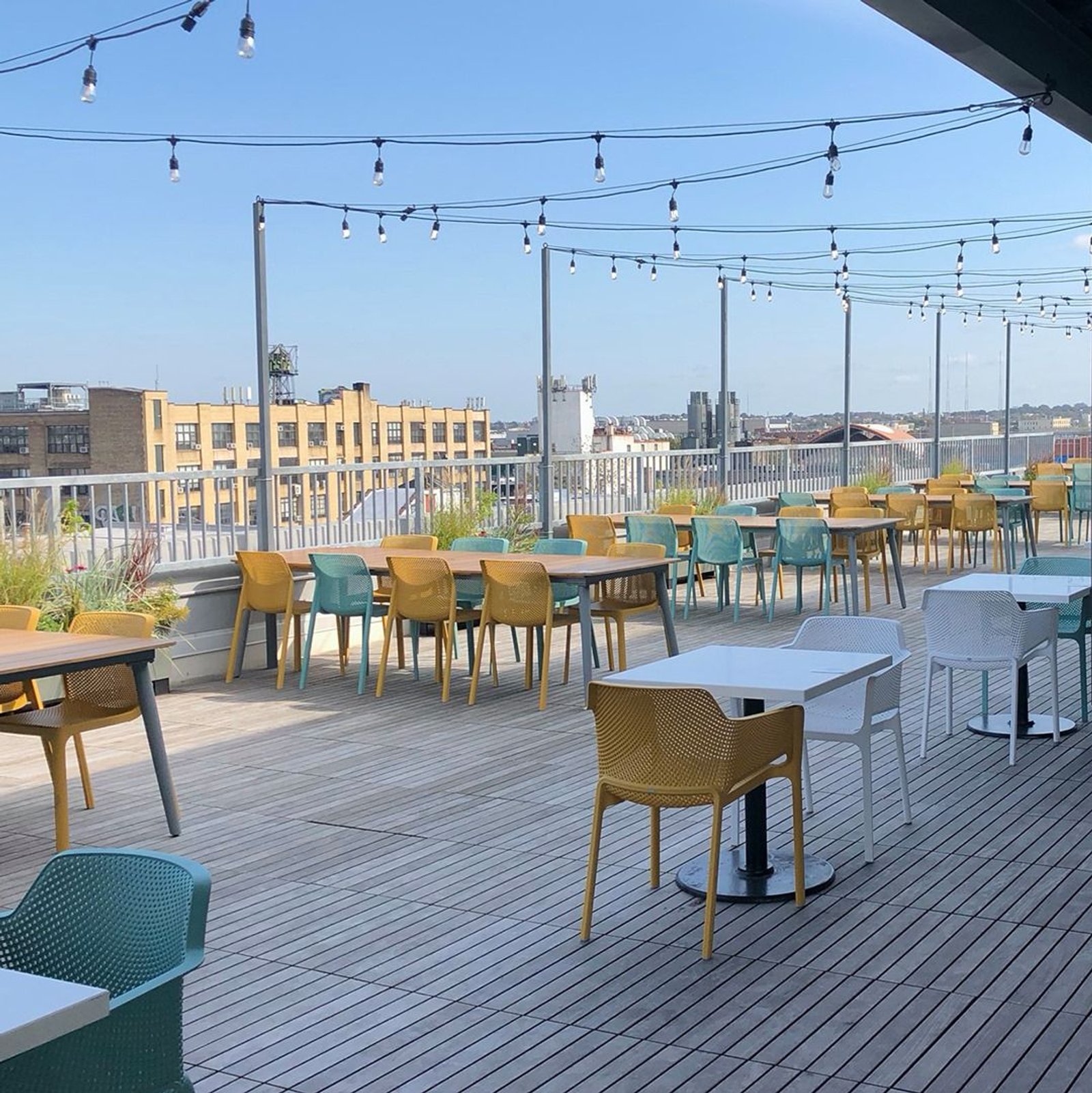 terraza de restaurante en rooftop con mesas, sillas amarillas y luces — proyecto Comedor, por Casa Nuñez