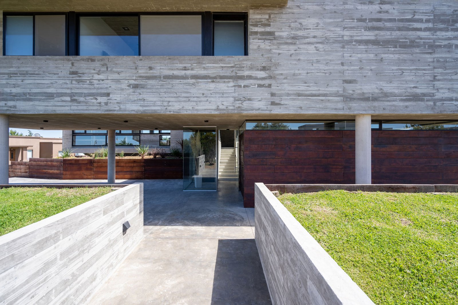 Fachada moderna de hormigón con detalles de madera y jardineras — proyecto Casa La Marina, por Besonías Almeida arquitectos, en X6VF+67