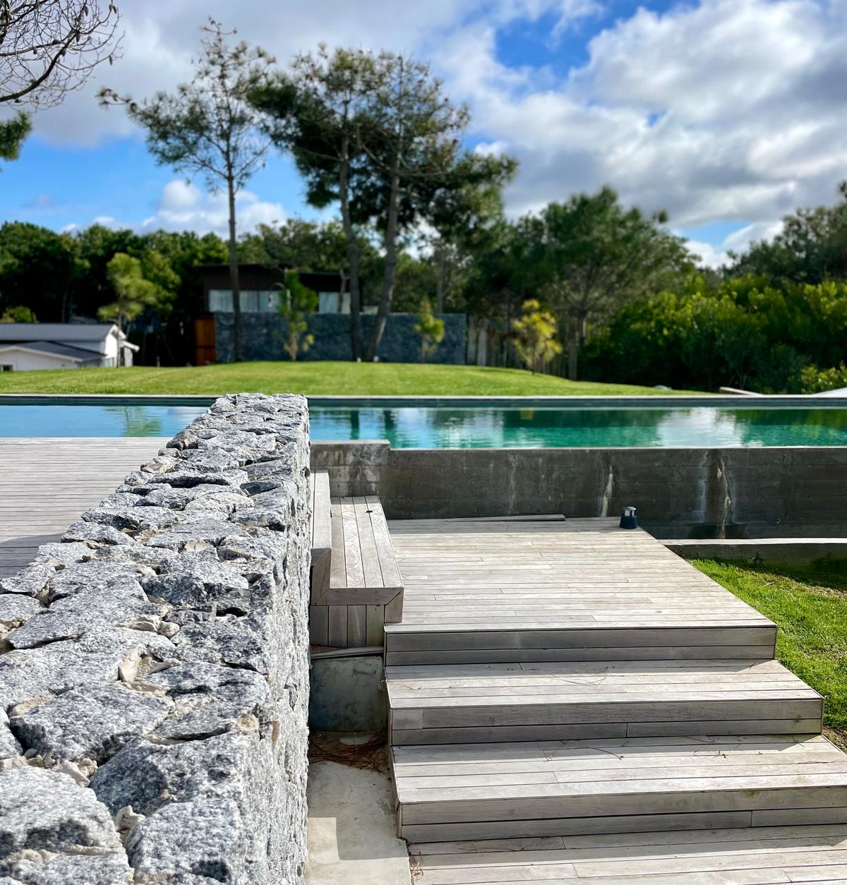 Piscina infinita com deck de madeira e muro de pedra — projeto CASA sobre el MAR, por Guerrero Arquitectos, em Pinamar