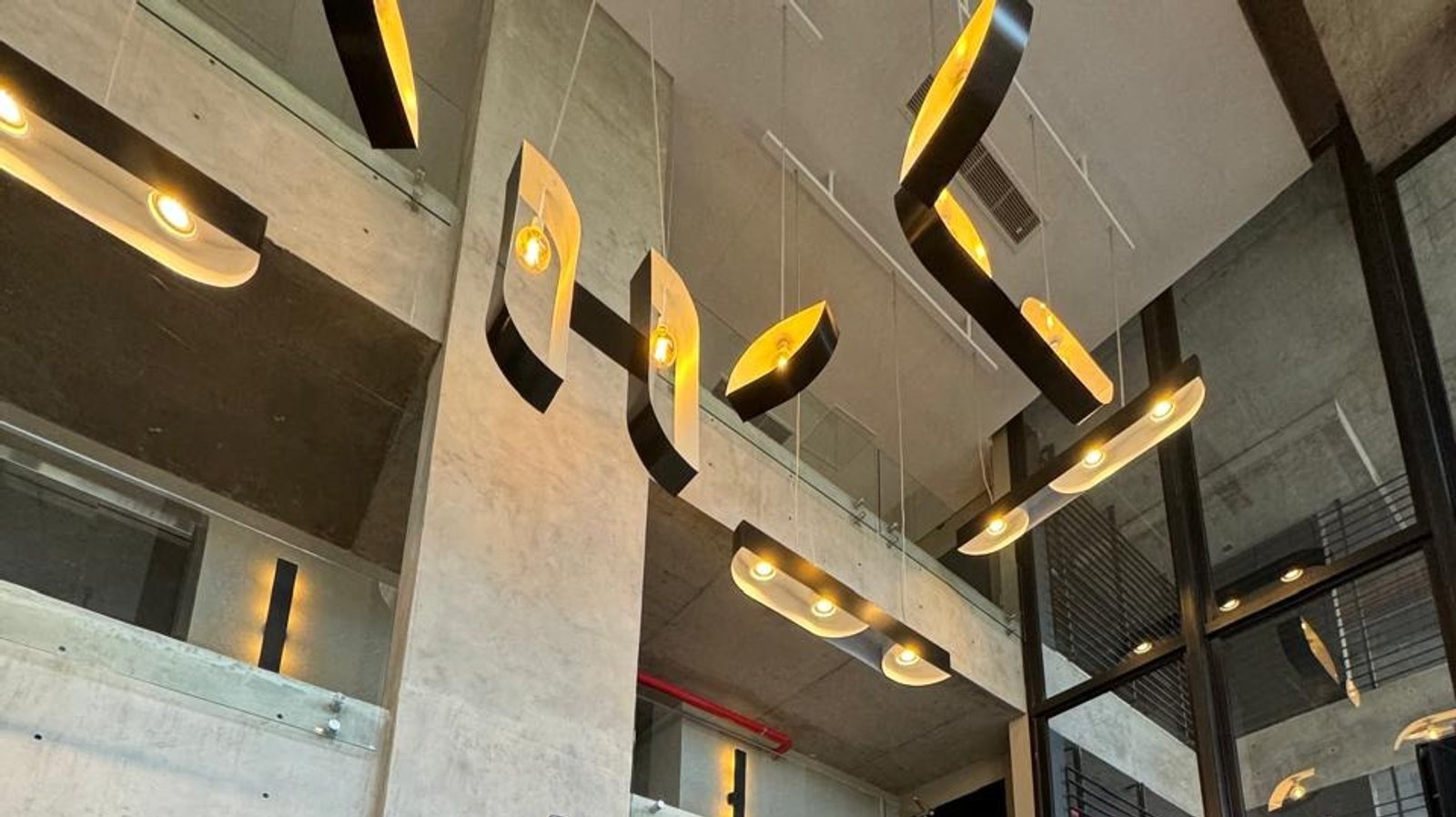 Iluminação pendente abstrata em corredor moderno de concreto — projeto UNDICI - Howard Johnson- La Boca, por COMOTTO - SOMMER  - ARQUITECTOS, em Brandsen 927