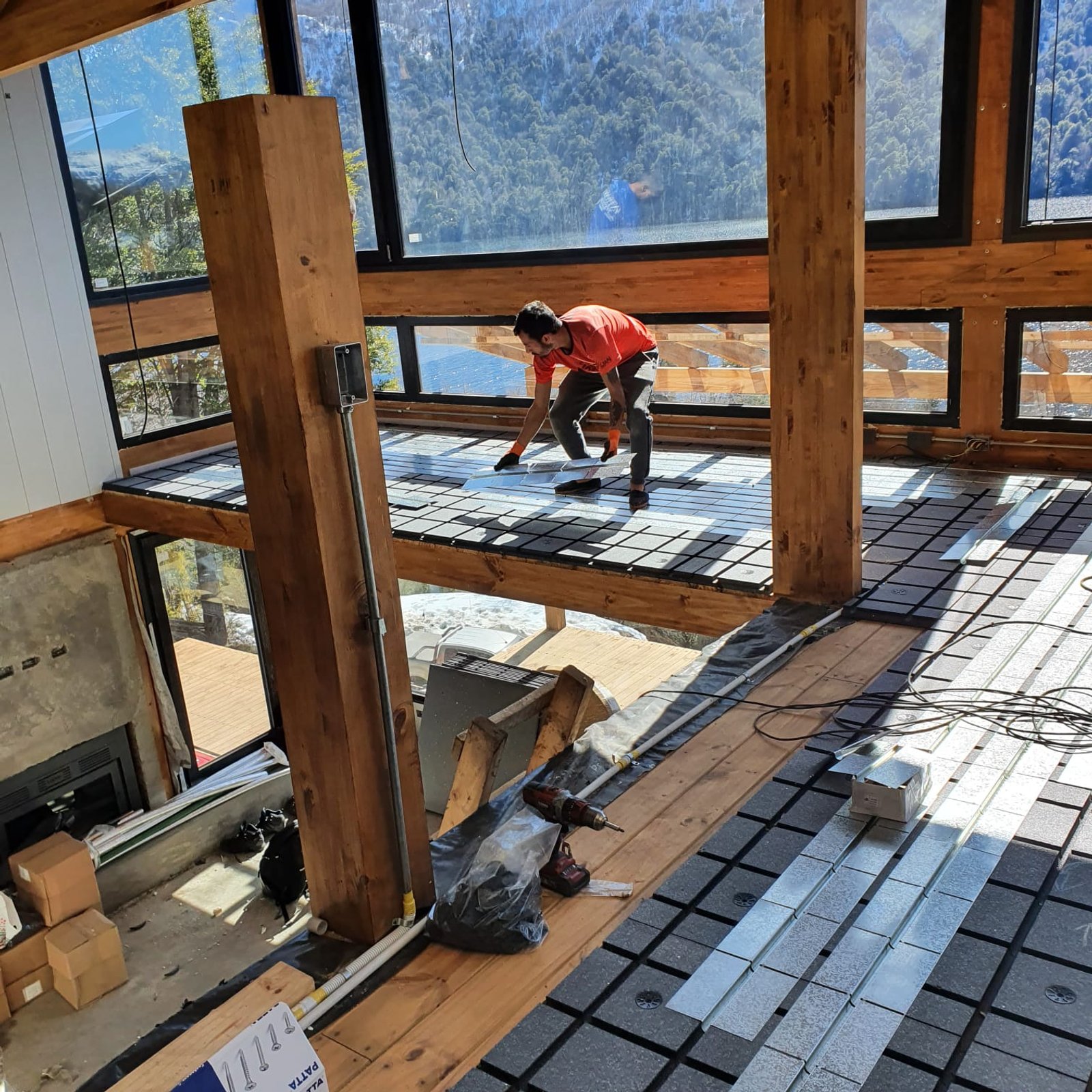 Interior em construção com vigas de madeira e vista para montanha — projeto Vivienda frente a Lago Hermoso, por TROKEN, em Neuquén