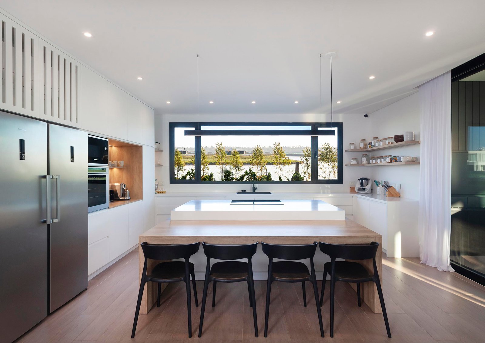 Cozinha moderna com ilha e vista externa por janelas amplas — projeto CASA C313, por A'PRIMA - Arquitectura Sustentable, em Provincia de Buenos Aires