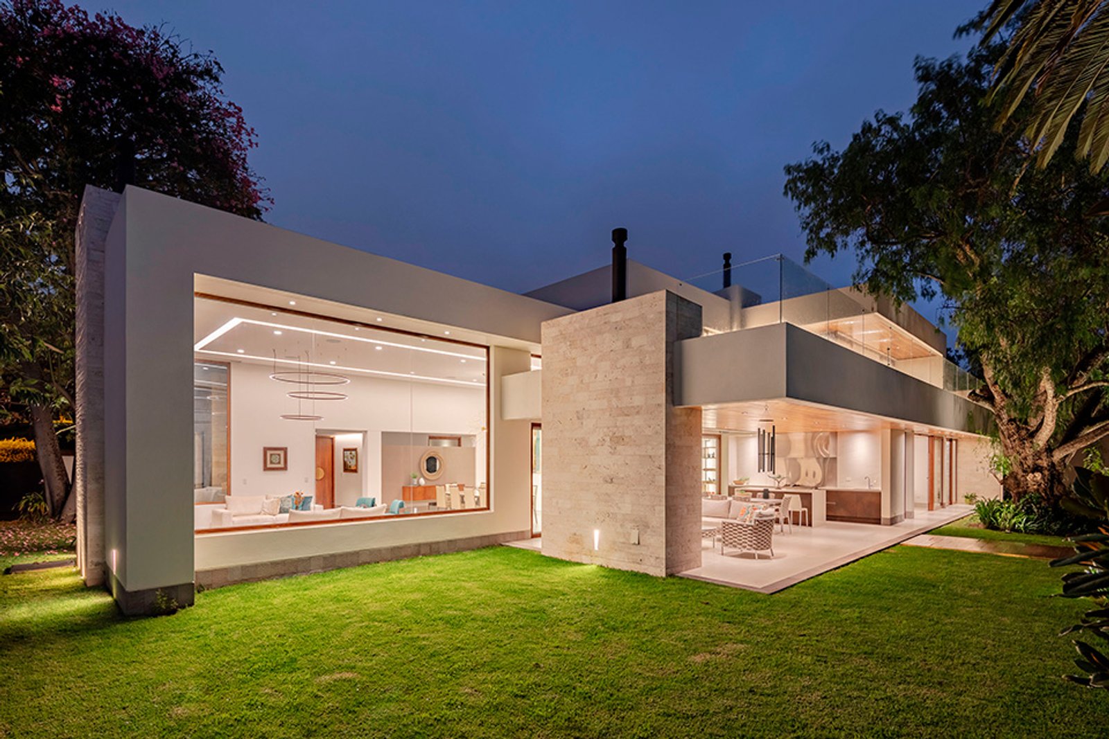 Fachada moderna con grandes ventanales iluminados de noche — proyecto Casa Molle, por MUCHTEK, en Cumbayá