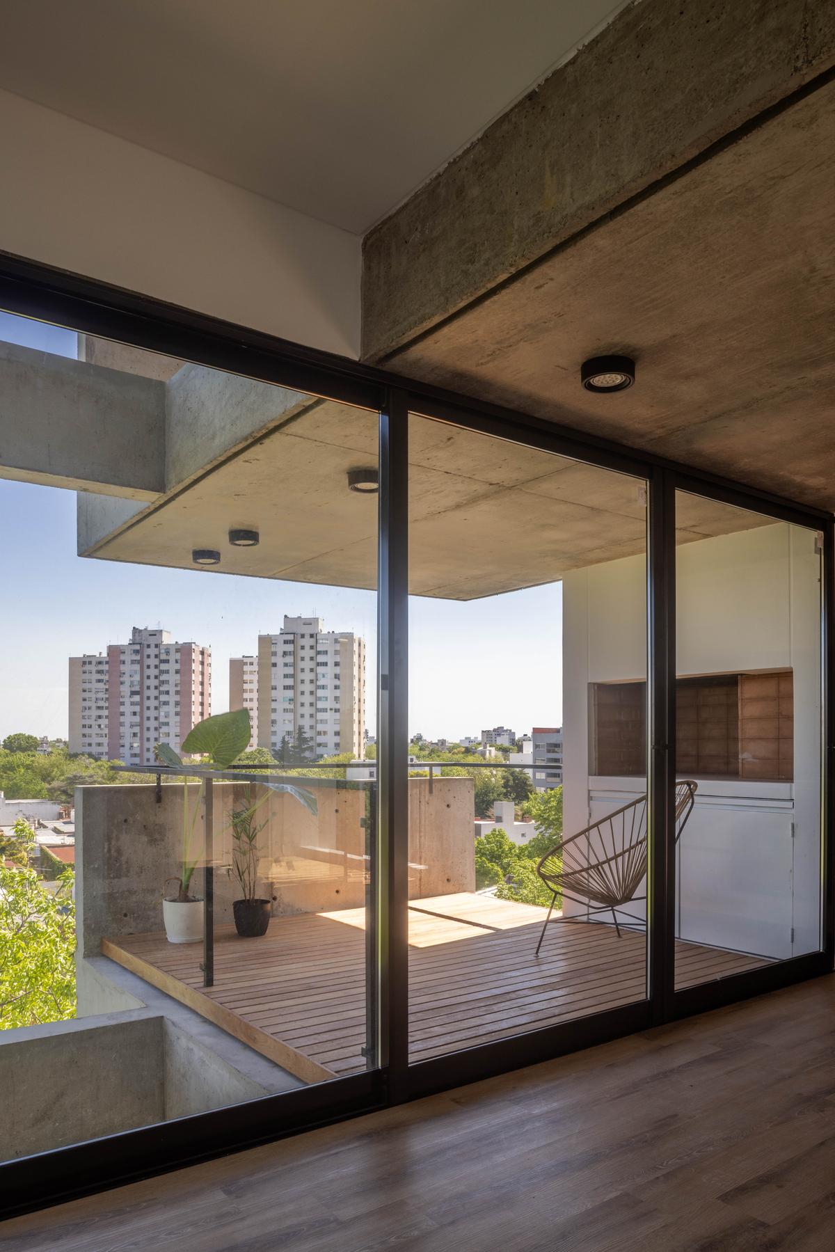 Varanda moderna com deck de madeira e concreto aparente — projeto Terrazas de Malvinas, por DREI Arquitectura y Desarrollos, em La Plata