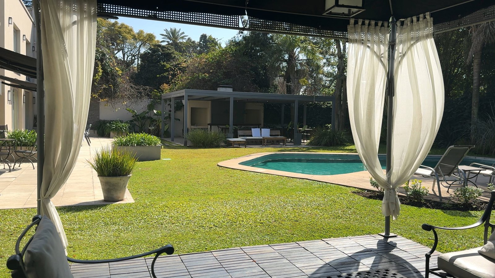 Terraço moderno com cortinas brancas, piscina e jardim exuberante — projeto Villa Isidro Hotel Boutique & Spa, por Hermann Arquitectos, em San Isidro