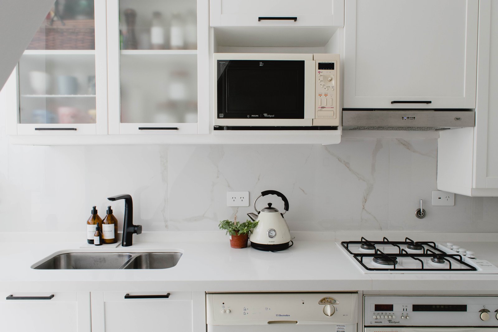 Cocina moderna blanca con electrodomésticos integrados y detalles en mármol — proyecto Goyena, por Martina Kleinert, en Caballito