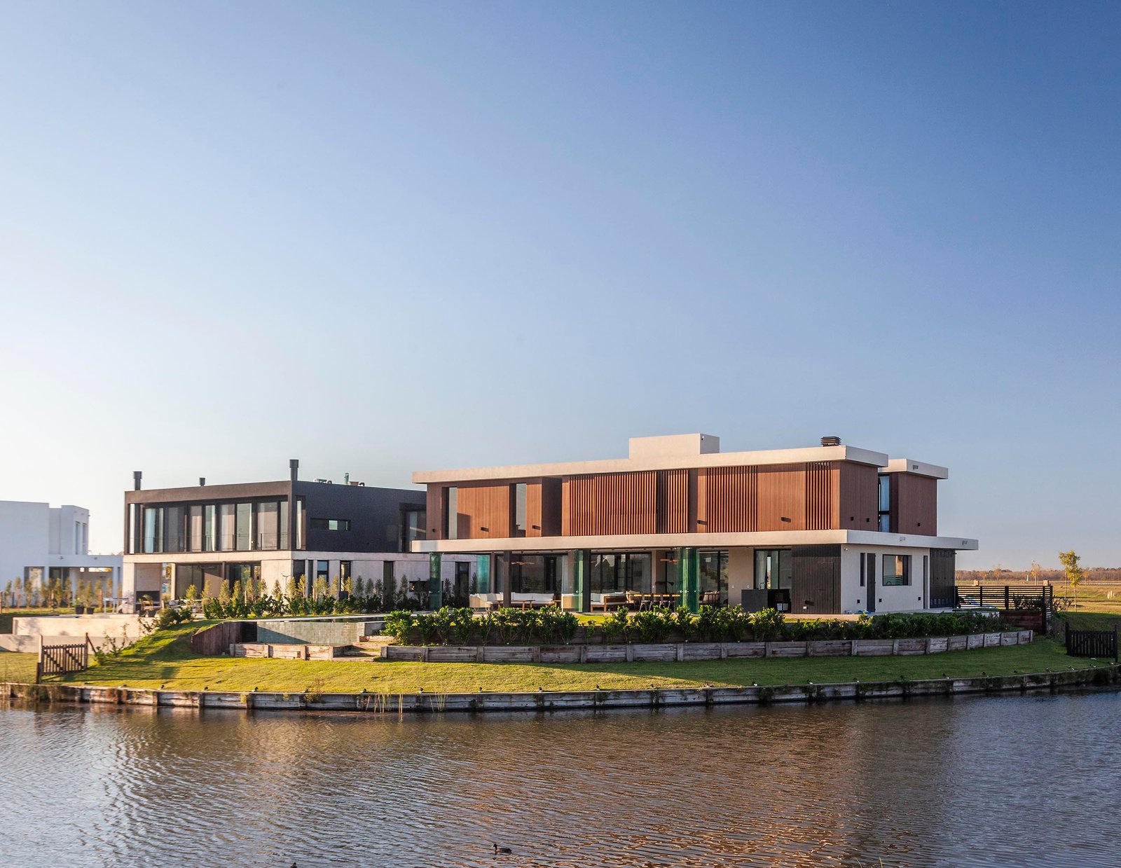 Fachada moderna junto al agua con detalles en madera — proyecto CASA C313, por A'PRIMA - Arquitectura Sustentable, en Provincia de Buenos Aires