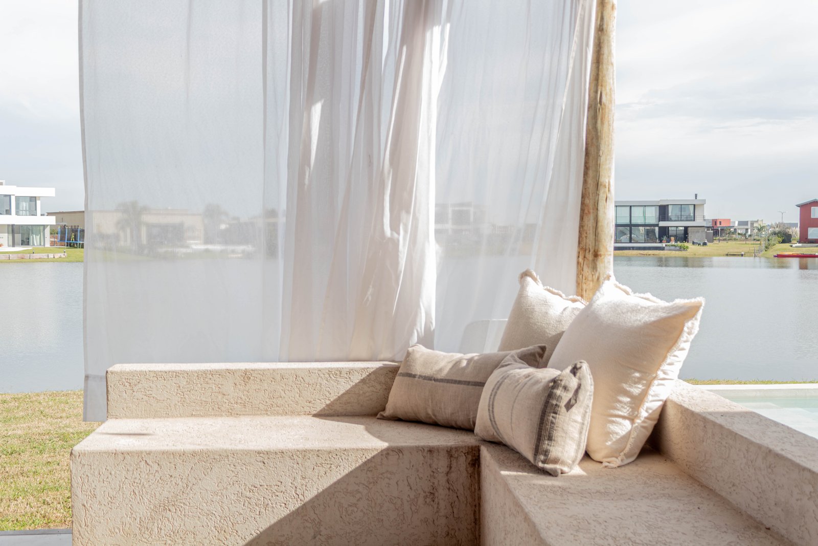Living exterior con sillones y cortinas blancas frente al agua — proyecto San Sebastian I, por Catalina Fitero Fotografìa, en M472+28