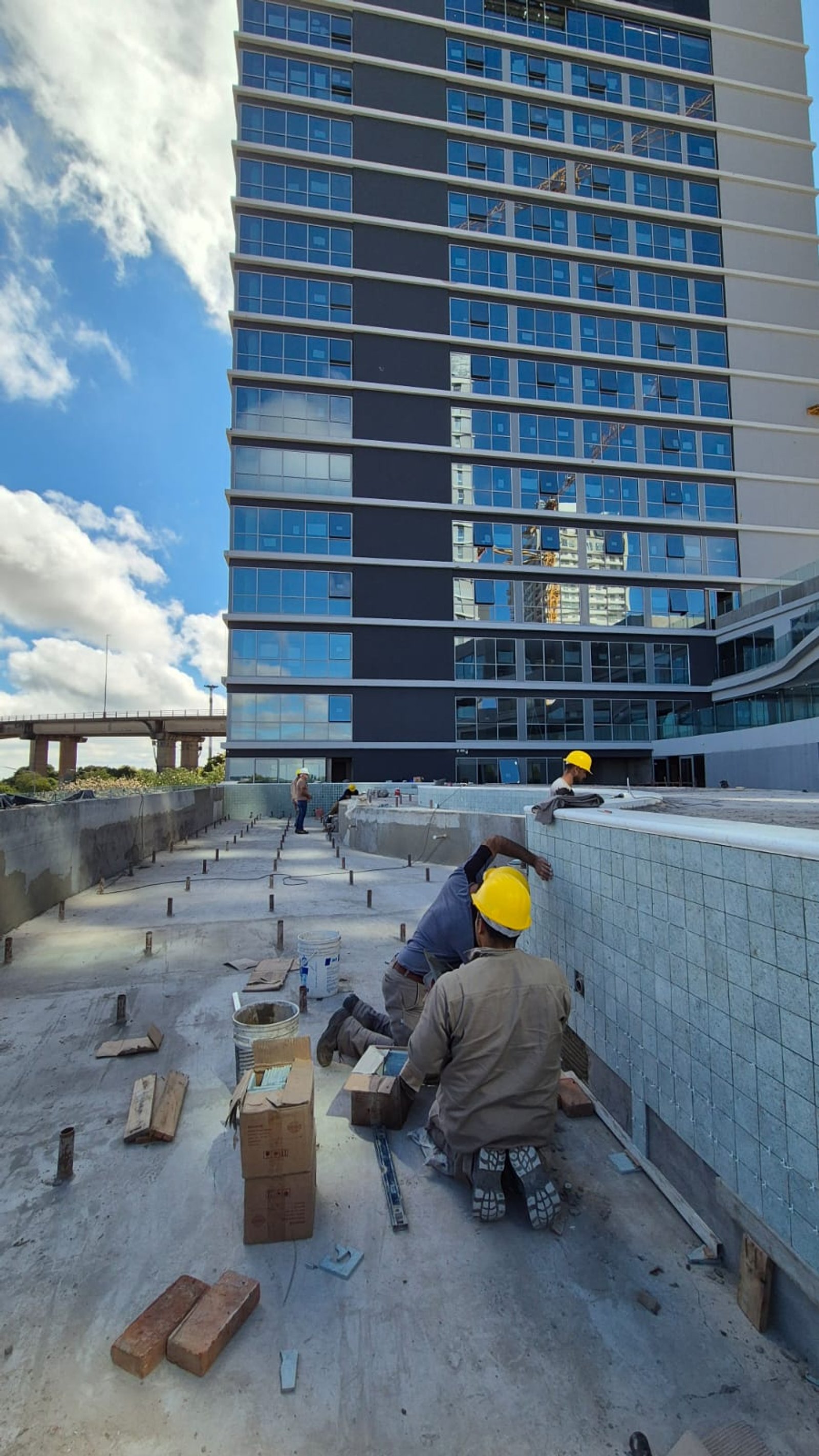 Construcción de piscina frente a edificio moderno con obreros — proyecto Obra Piscina Los Boulevares Corrientes en Proceso, por Aquamare Piscinas, en Corrientes