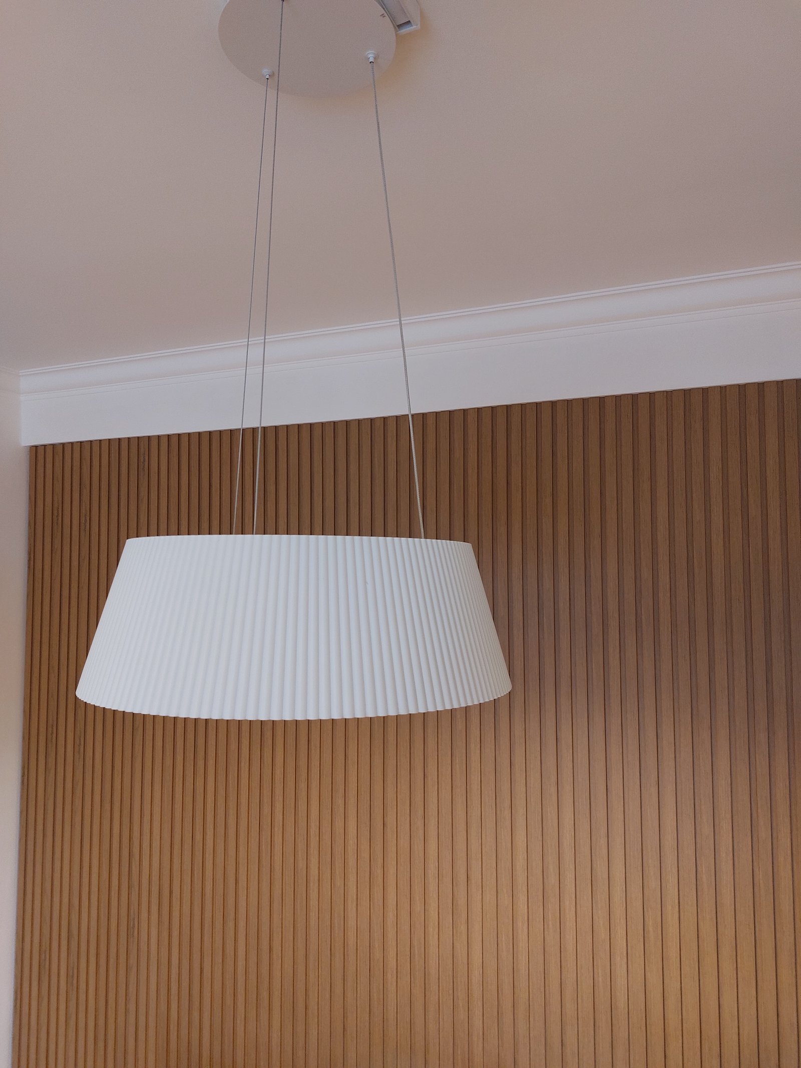 Lámpara colgante cónica con pantalla plisada sobre pared de listones de madera — proyecto FLORES, por Arquitecta, en Flores