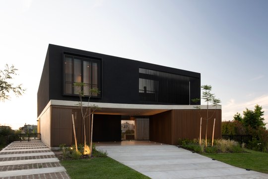 fachada moderna con volúmenes geométricos en negro y madera — proyecto Obra Muelles, por lifecycle, en Av. de los Lagos