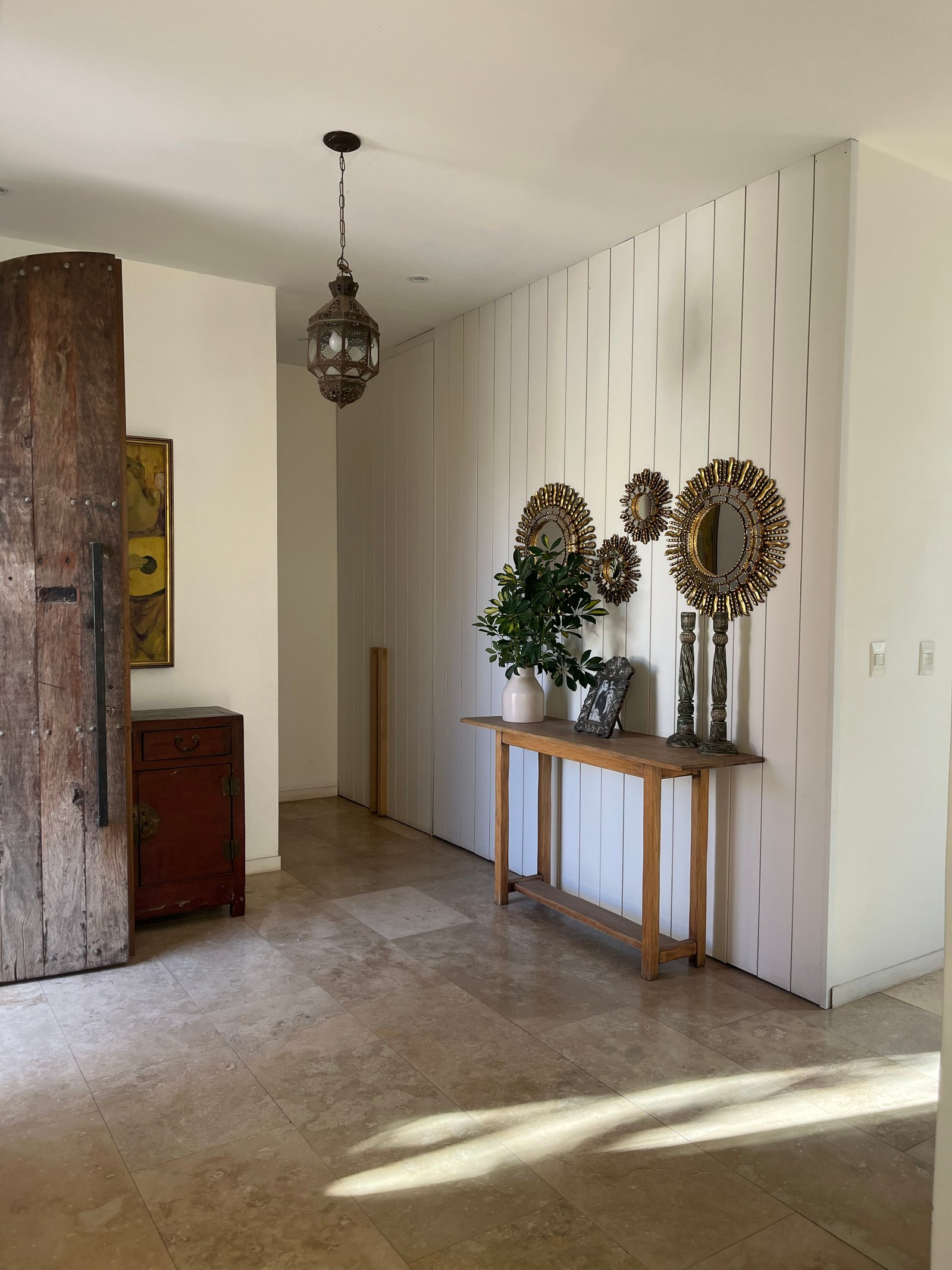 Pasillo rústico con puerta de madera antigua y espejos solares — proyecto Casa Montevideo, por R+B arquitectos, en Bella Vista