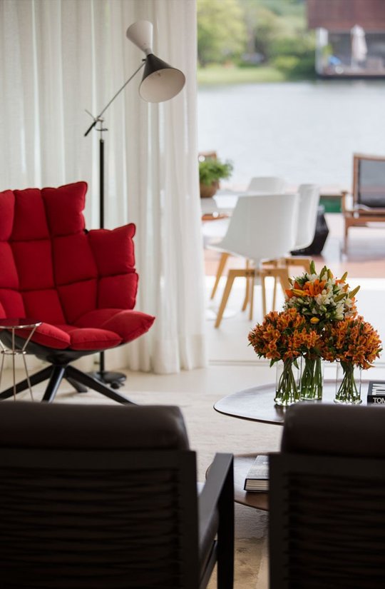 Living moderno con sillón rojo, vista al río y flores naranjas — proyecto Arquitetura e Interiores II, por Demian Golovaty