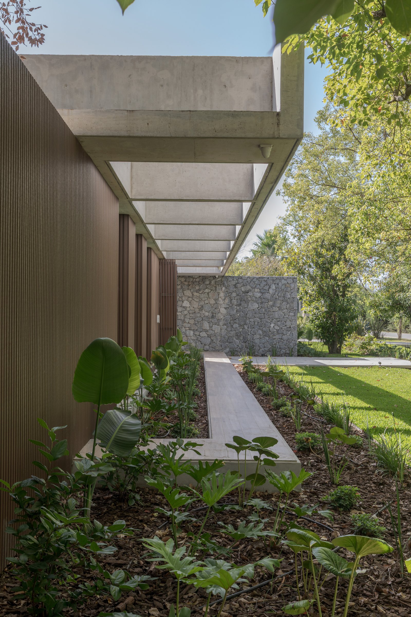 Fachada moderna con pérgola de hormigón y jardín exuberante — proyecto Casa PLANALTO, por Grupo CRBN, en Av. Pres. Perón 10298