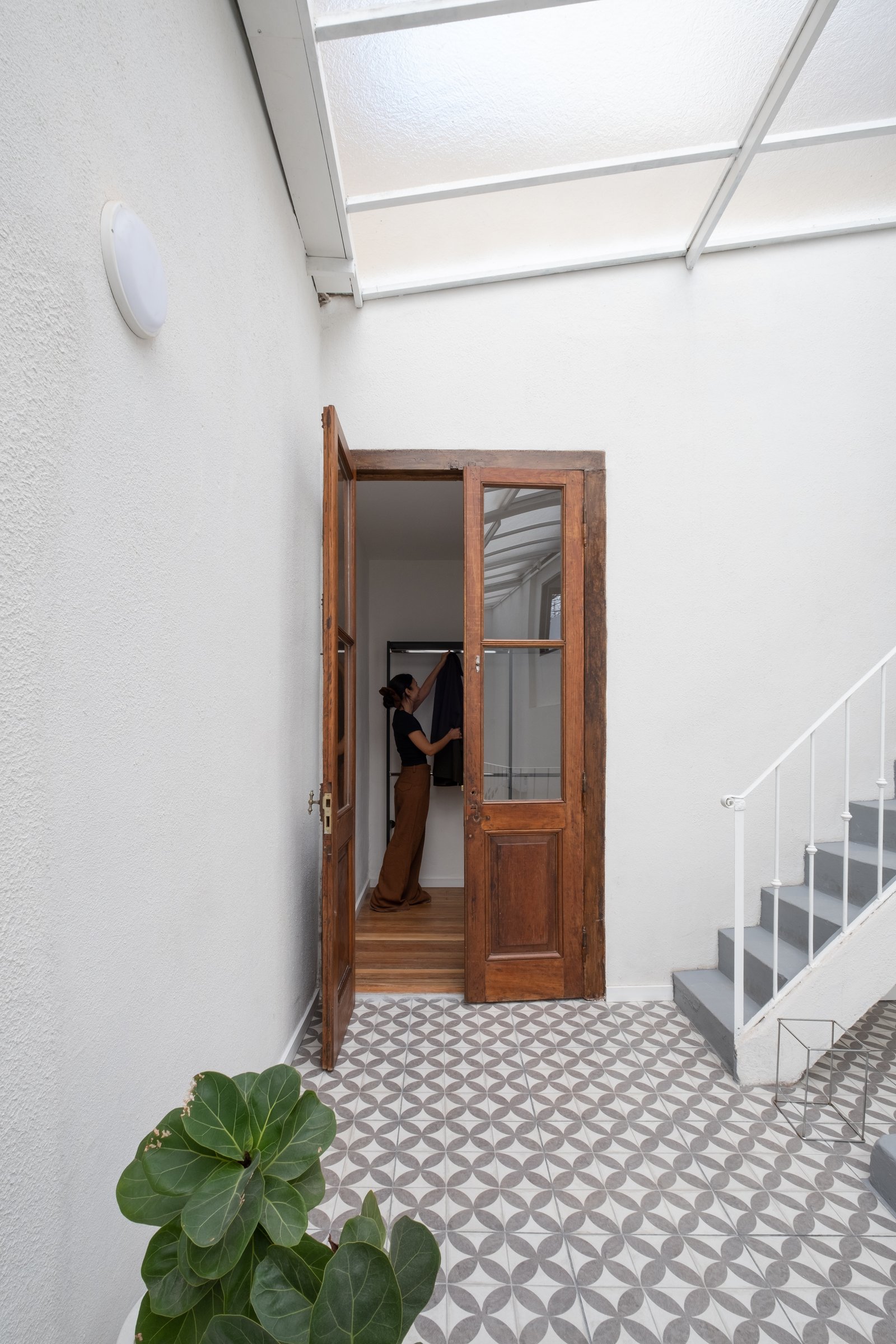 Corredor com piso de ladrilhos estampados, escada e porta dupla de madeira aberta — projeto Casa Patio, por Herrera Ungaro, em San Cristóbal