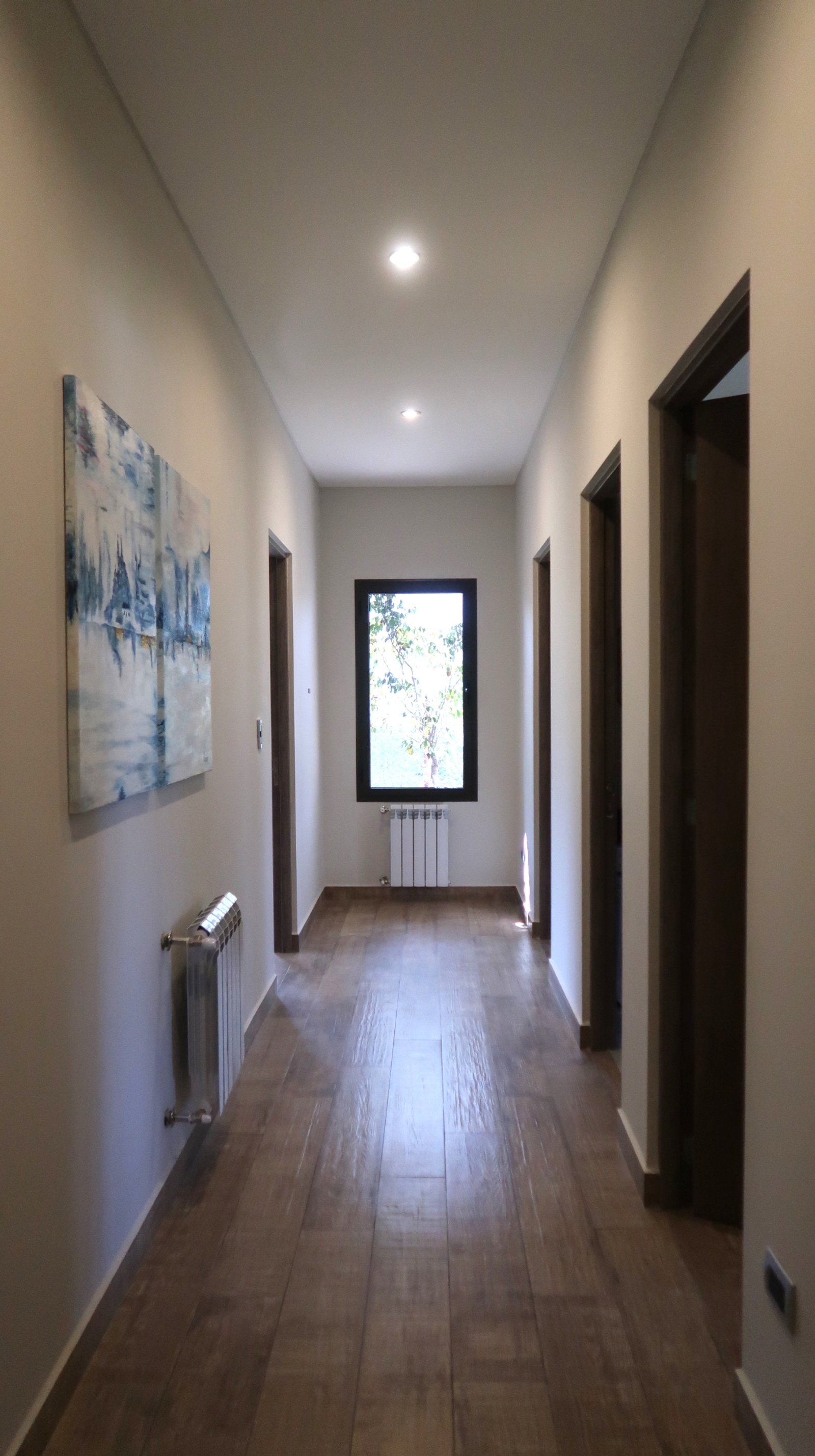 Corredor moderno com obra de arte e piso de madeira — projeto Casa La Paz, por Luciana González Anderson, em Salta