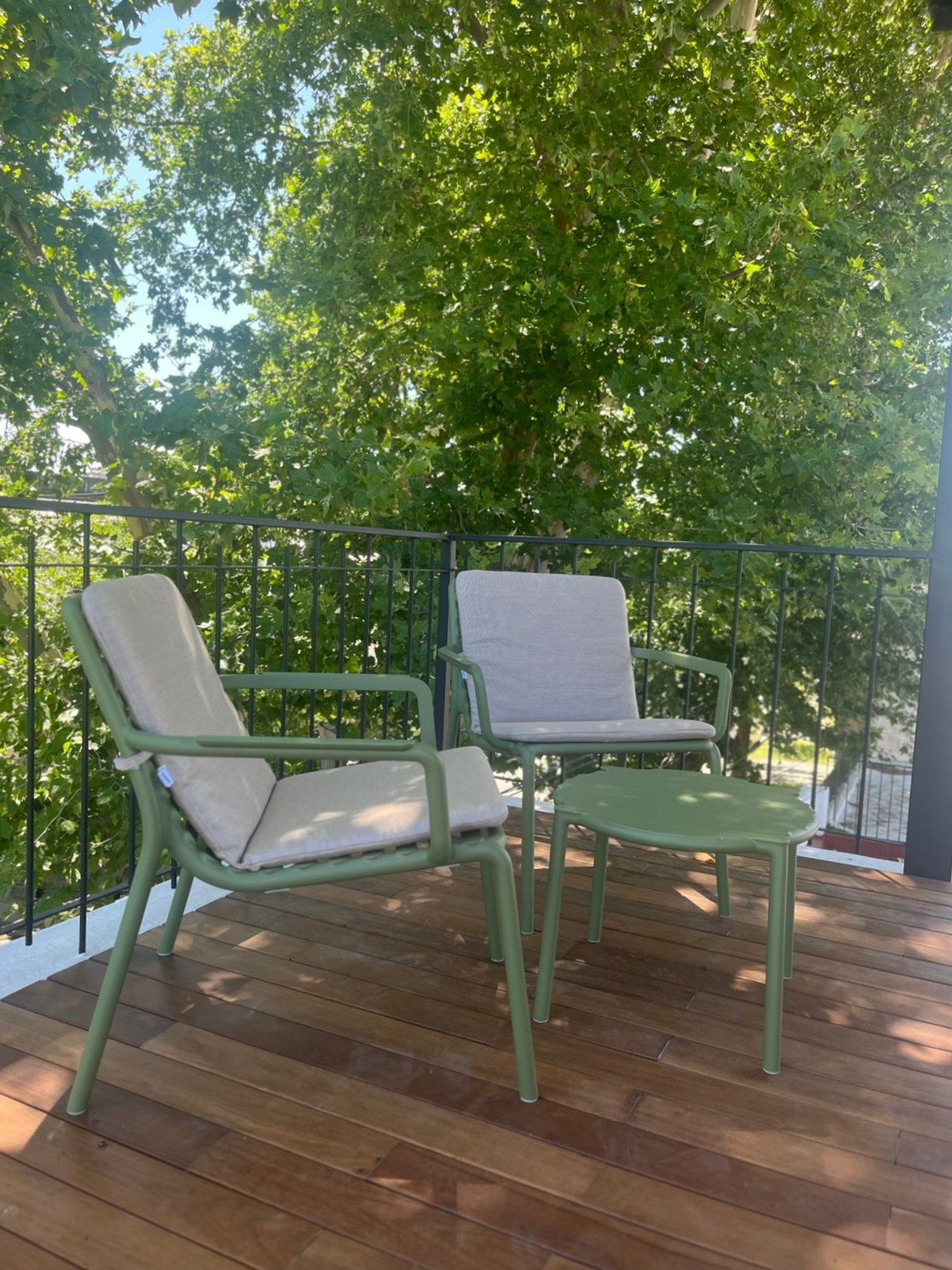 Balcón con sillones verdes, mesa y deck de madera, rodeado de árboles — proyecto Balcón y Terraza, por Casa Nuñez