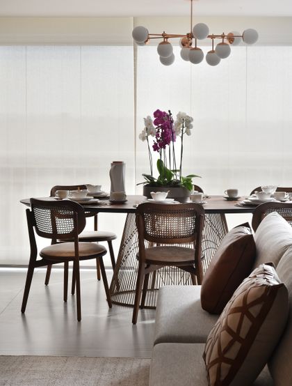 Comedor moderno con sillas de rattan, mesa oscura y orquídea púrpura — proyecto Apartamento DE, por Giovana Ciacco, en Guarulhos