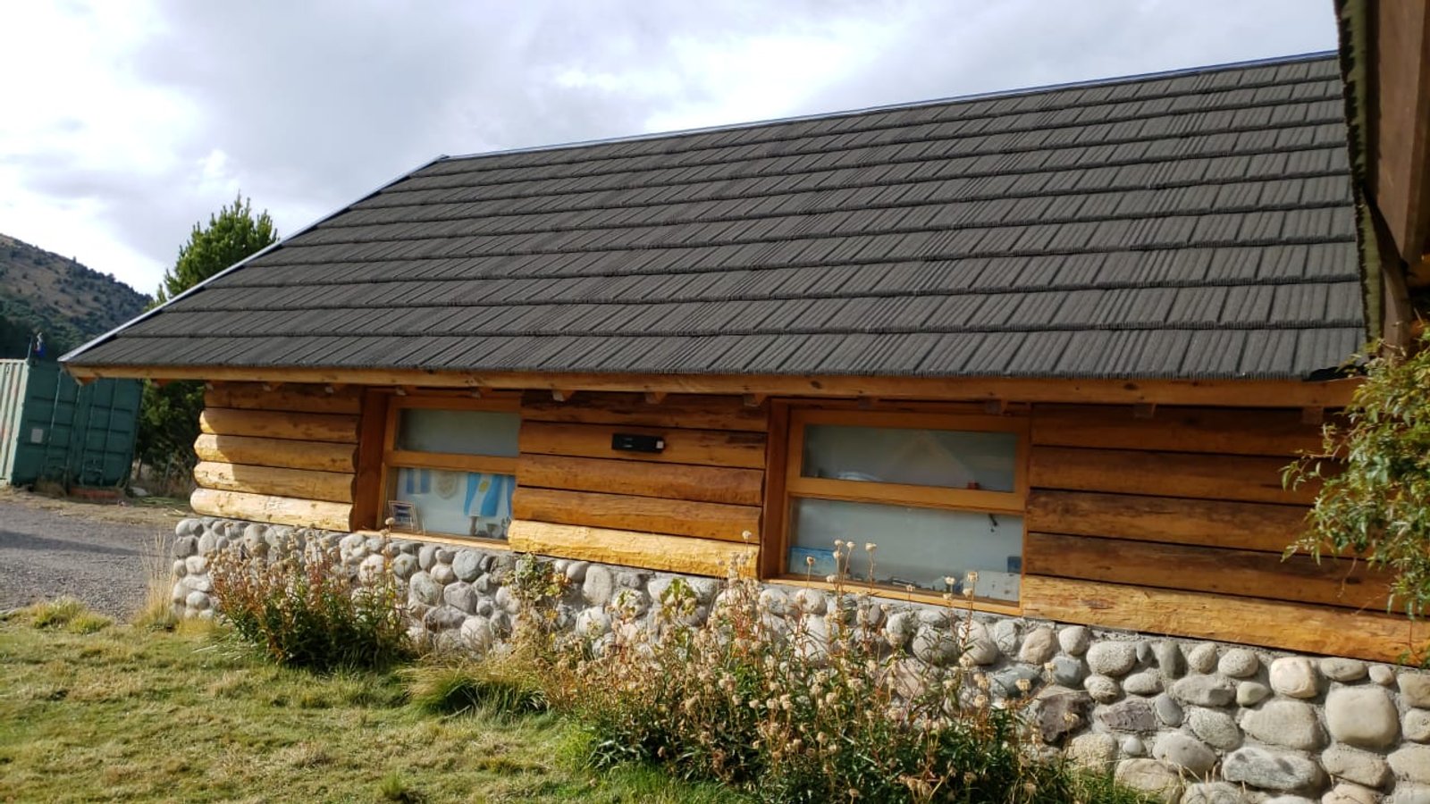 fachada de cabaña rústica de troncos con cimientos de piedra — proyecto Teja Gravillada., por Yrigoyen Construcciones, en Córdoba