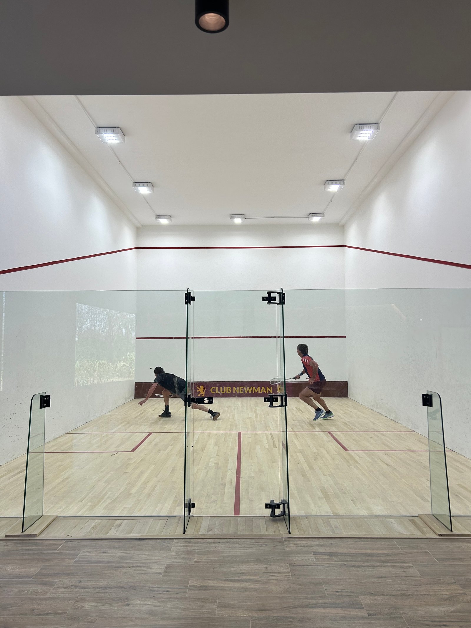 Cancha de squash de cristal con jugadores en acción — proyecto SQUASH CLUB NEWMAN, por ESTUDIO TEZ, en Benavidez