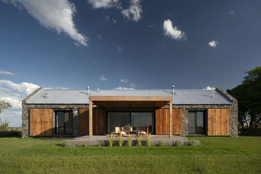 Fachada moderna de piedra y madera con pérgola y patio central — proyecto Campo Cria , por Estudio Lak