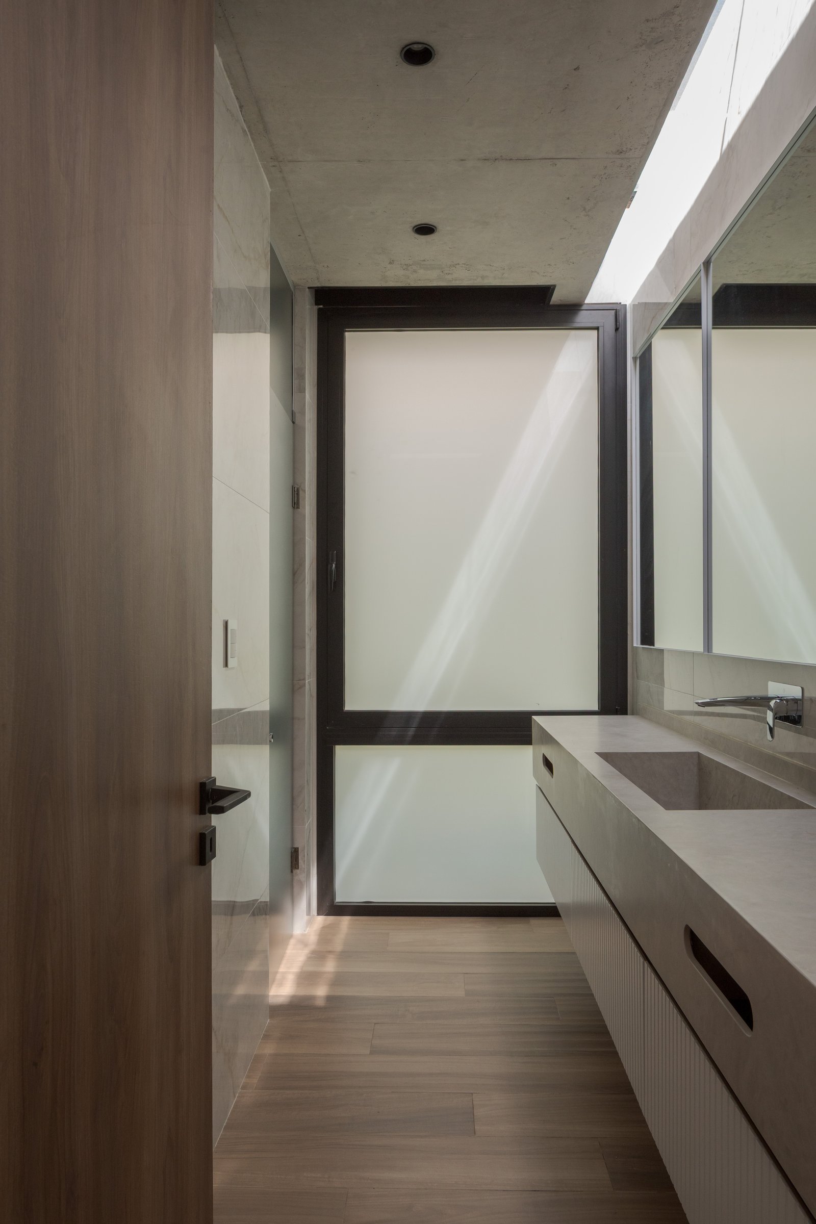 Baño moderno con techo de hormigón, luz cenital y lavabo de piedra — proyecto Casa PLANALTO, por Grupo CRBN, en Av. Pres. Perón 10298