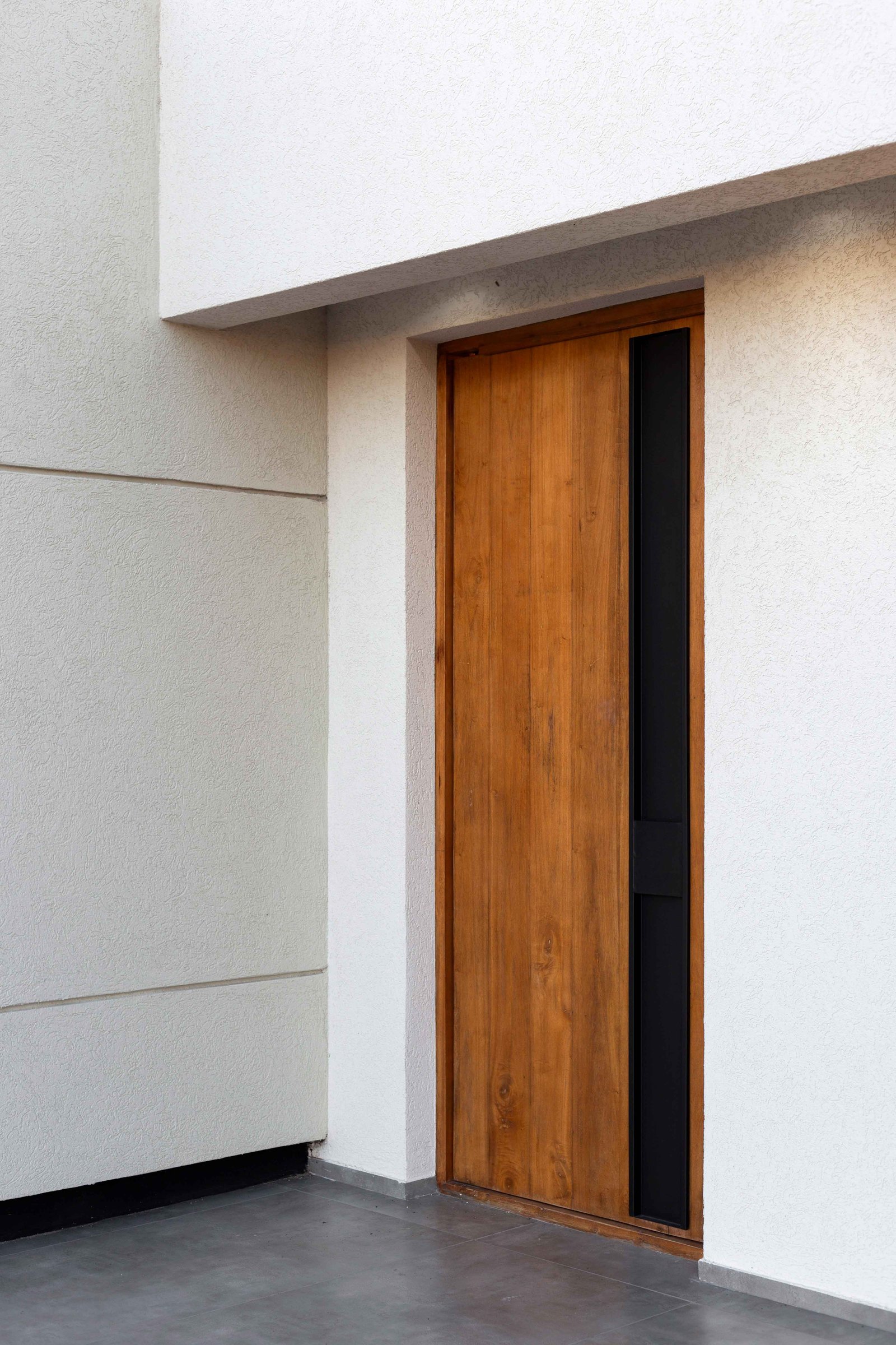 fachada moderna con puerta de madera y detalles oscuros — proyecto San Simon I, por Estudio Stepa, en Ezeiza