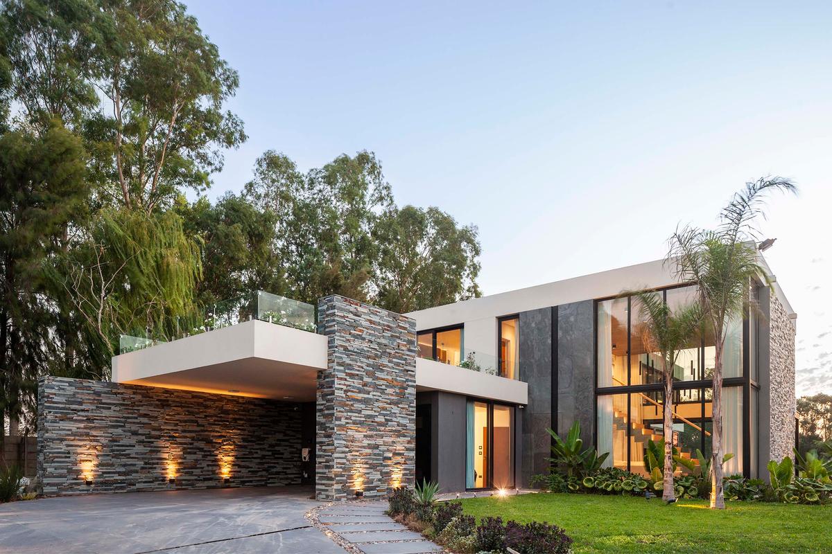 fachada moderna de dois andares com pedra, madeira e vidro — projeto CASA T199, por A'PRIMA - Arquitectura Sustentable, em Los Robles 5901