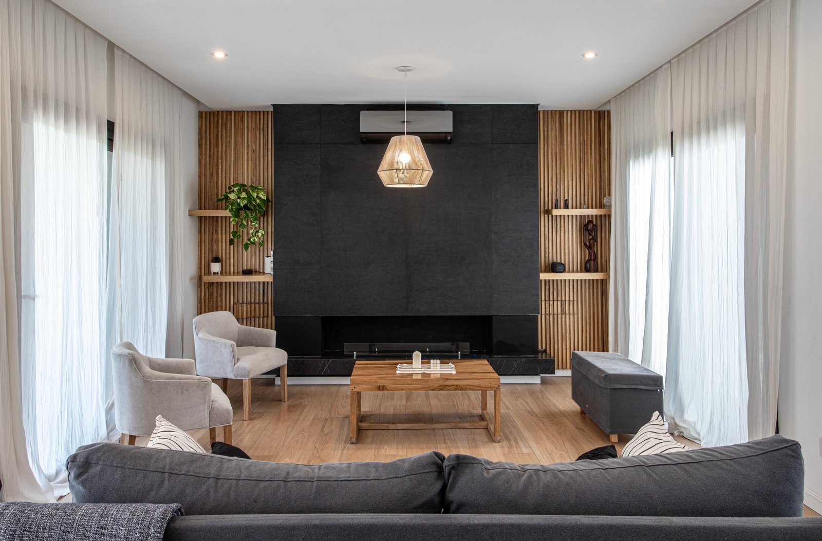 Sala de estar moderna con chimenea de piedra negra y detalles en madera — proyecto SS45, por EZ architects, en Pilar