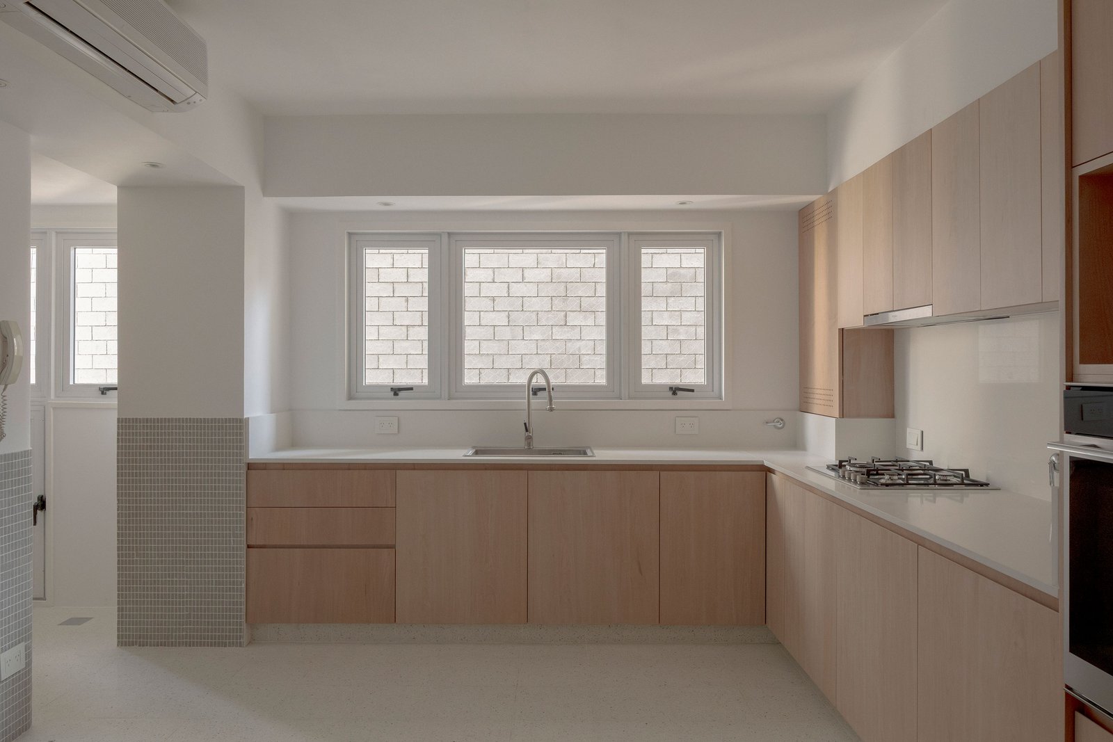 Cozinha minimalista com armários de madeira clara e bancadas brancas — projeto Reforma O'Higgins, por Estudio YME, em Belgrano