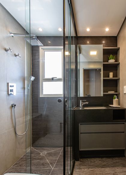Baño moderno con ducha vidrio, mesada negra y estanterias flotantes — proyecto Duo Morumbi 2, por Pricila Dalzochio