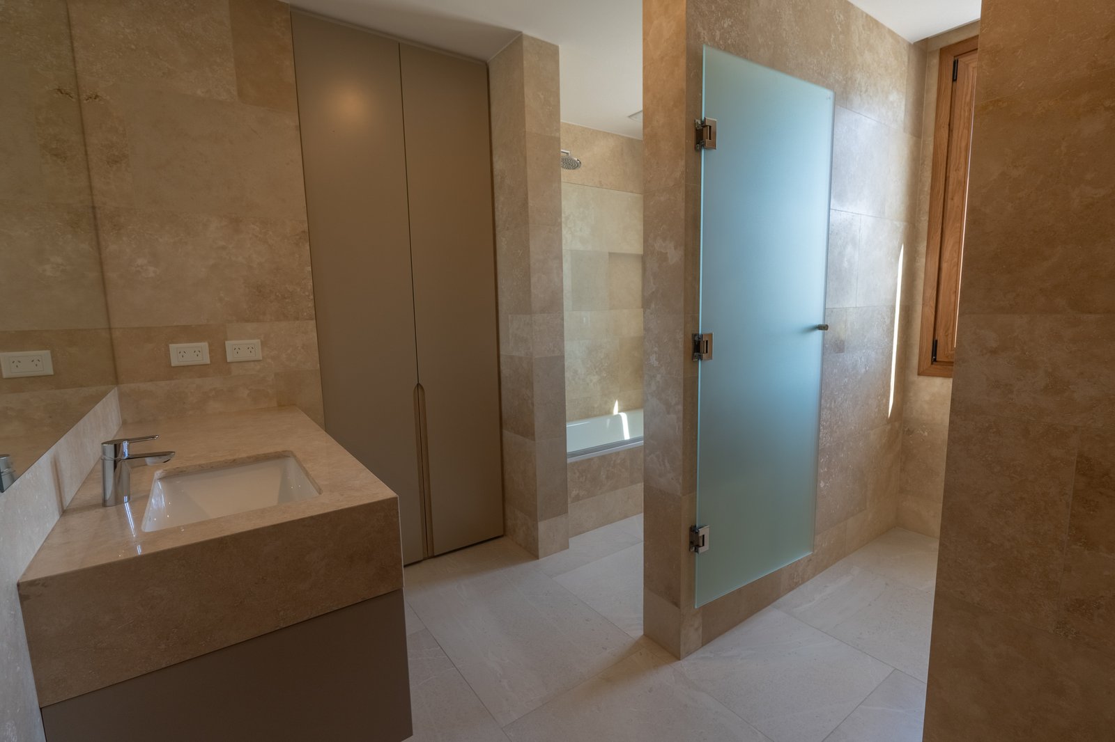 Baño moderno con revestimiento de piedra beige y puerta de ducha de vidrio esmerilado — proyecto LOTE 004, por DIKKA Arquitecta , en San Vicente
