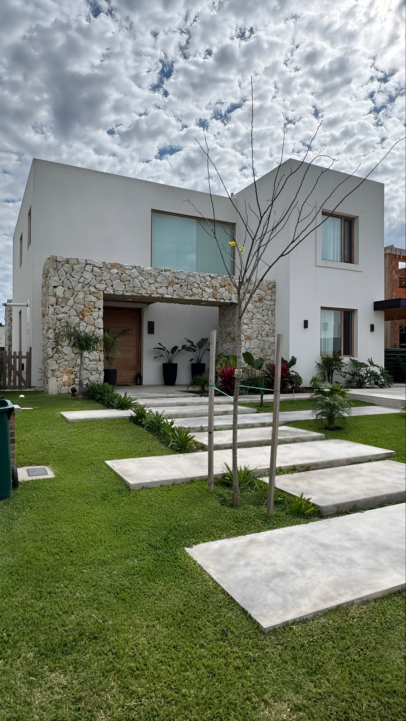 Fachada moderna con entrada de piedra, césped y camino de baldosas de hormigón — proyecto Casa ER , por Hermann Arquitectos, en Arribeños 1611