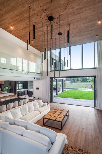 Sala de estar moderna de doble altura con vistas al jardín y lámpara colgante escultórica — proyecto CASA T199, por A'PRIMA - Arquitectura Sustentable, en Los Robles 5901