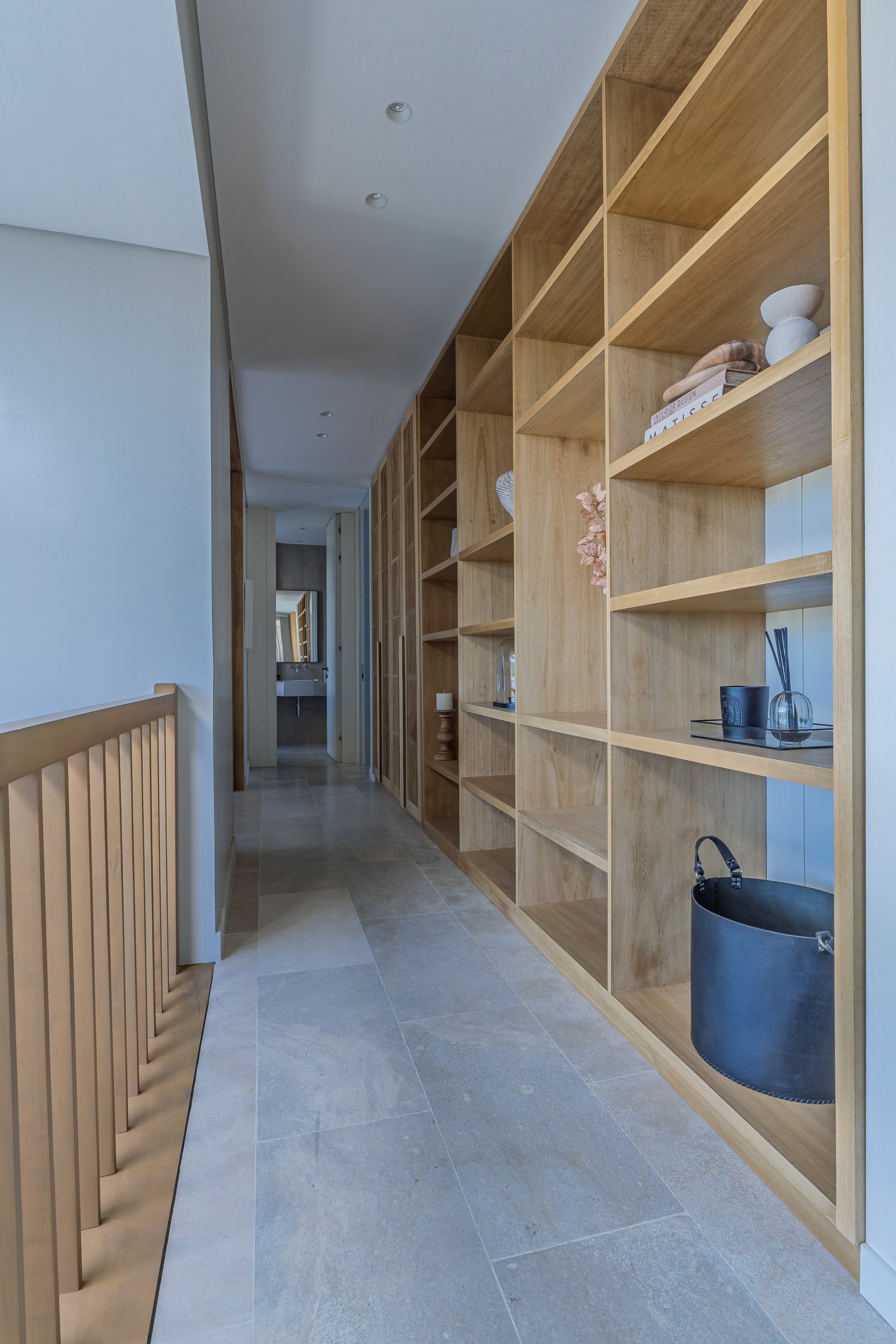 Pasillo largo con estanterías de madera y piso de piedra gris — proyecto Pilar A, por Josefina Bertora, en Los Cipreses 2