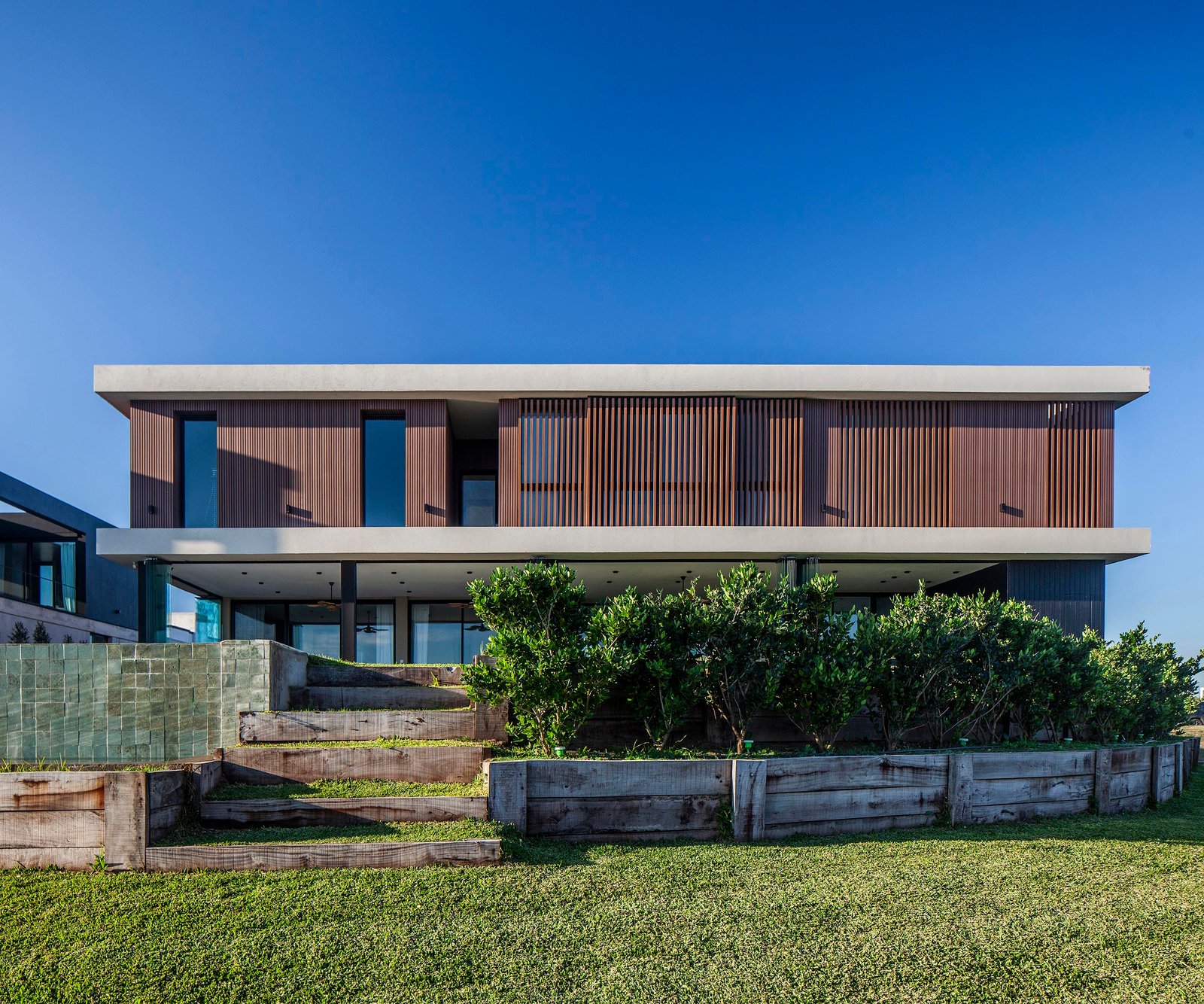 Fachada moderna de casa residencial con revestimiento de madera y concreto frente al mar — proyecto CASA C313, por A'PRIMA - Arquitectura Sustentable, en Provincia de Buenos Aires