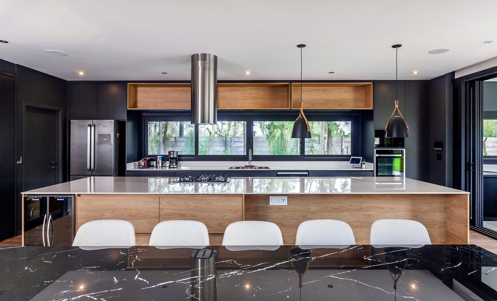 Cocina moderna con isla central, gabinetes de madera oscura y luces geométricas — proyecto CASA T199, por A'PRIMA - Arquitectura Sustentable, en Los Robles 5901