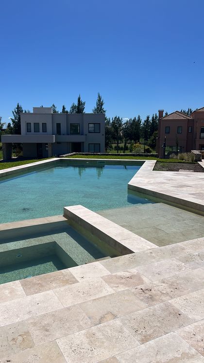 Pileta en obra con deck de piedra y casa minimalista blanca — proyecto CASA LR 456 - SOFITEL LOS CARDALES, por Carolina Depetris, en B2814 Los Cardales