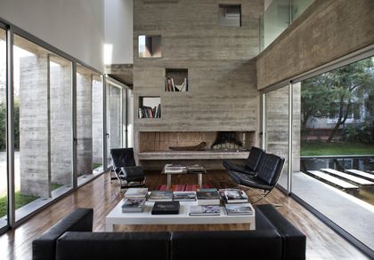 Living con doble altura, hogar central y amplios ventanales al jardin — proyecto Casa Torcuato, por Luciano Kruk