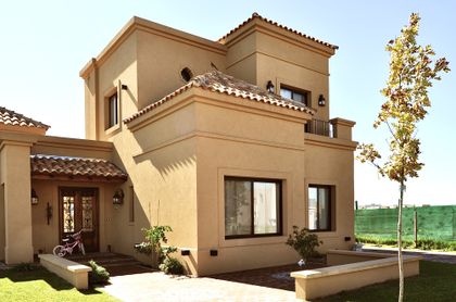 Fachada residencial estilo mediterráneo beige con techos de terracota y jardín — proyecto San Marcos, por Marconi Silva Arquitectos, en Benavidez