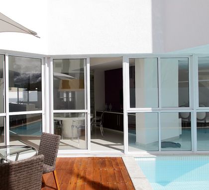 Pileta con deck de madera frente a galería vidriada moderna — proyecto Casa em Garanhuns Pernambuco, por André Caricio