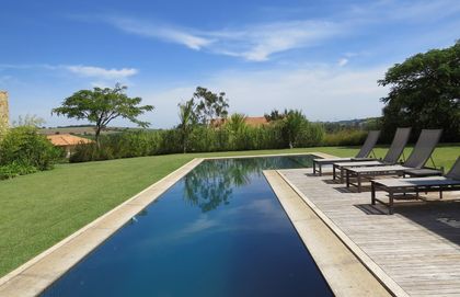 Pileta espejo con deck de madera y jardín verde extenso — proyecto Residencia PZ, por Gil Fialho