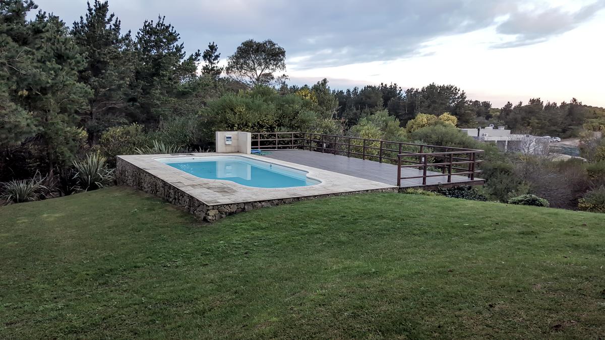 Piscina moderna cercada por vegetação exuberante com deck de madeira — projeto Vivienda Unifamiliar en Costa Esmeralda, por Estudio Schifano, em Costa Esmeralda