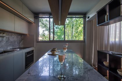 Cocina moderna con isla de mármol gris y grandes ventanales verdes — proyecto Residencia TS, por Karina Vinocur